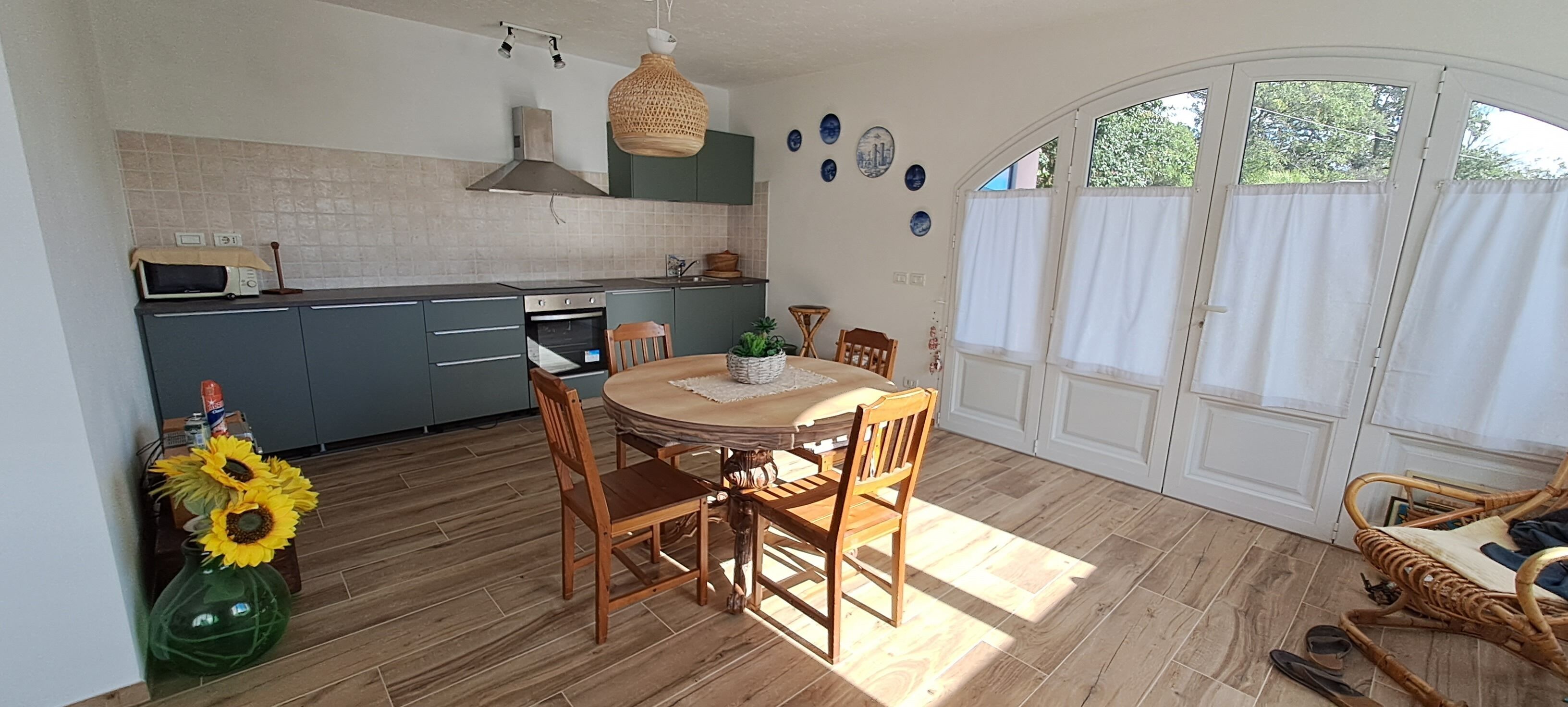Une cuisine avec un coin repas, un plancher en bois et une grande fenêtre avec des rideaux.