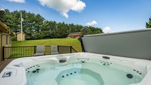 Un jacuzzi con un deck cubierto de césped y sillas, rodeado por una valla y árboles.