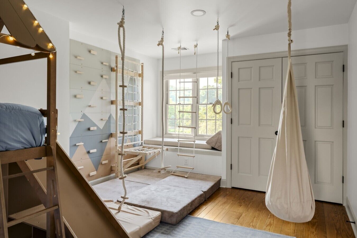 Une chambre avec un lit superposé, une échelle de corde, un hamac, une fenêtre donnant sur un beau paysage et une porte.