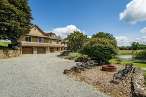 Une maison à deux étages, avec des fondations en pierre, une allée en gravier et un étang entouré d’une clôture.