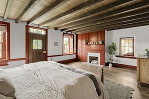 Une chambre avec un grand lit, des poutres en bois, une cheminée et une fenêtre.