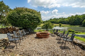 Un espace extérieur aménagé avec des chaises et un foyer, entouré d’arbres et offrant une vue sur le lac.