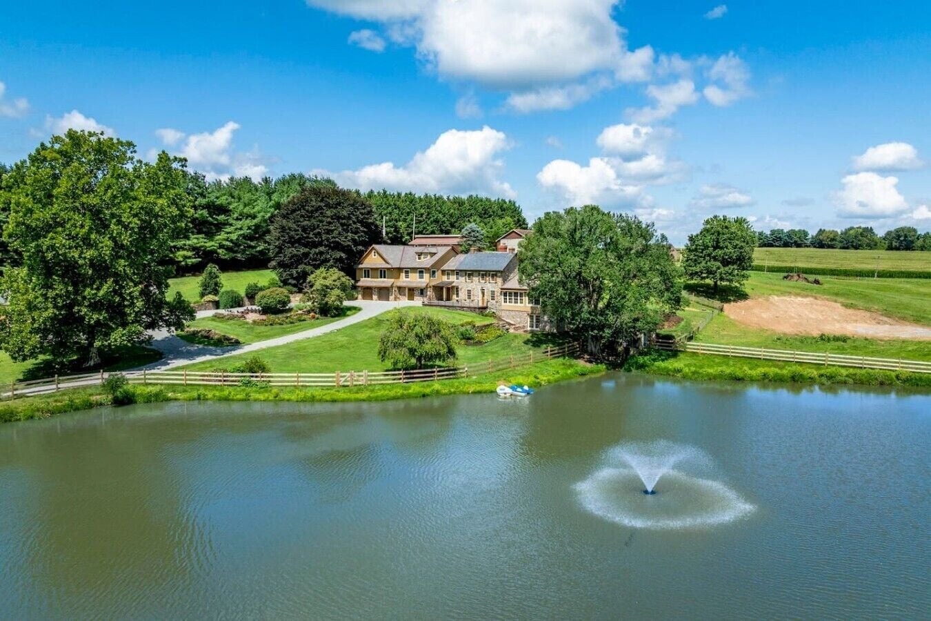 Ein großes Haus mit Teich im Vordergrund, umgeben von Bäumen und blauem Himmel.