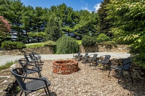 An outdoor seating area with chairs and a fire pit surrounded by trees and a stone wall.