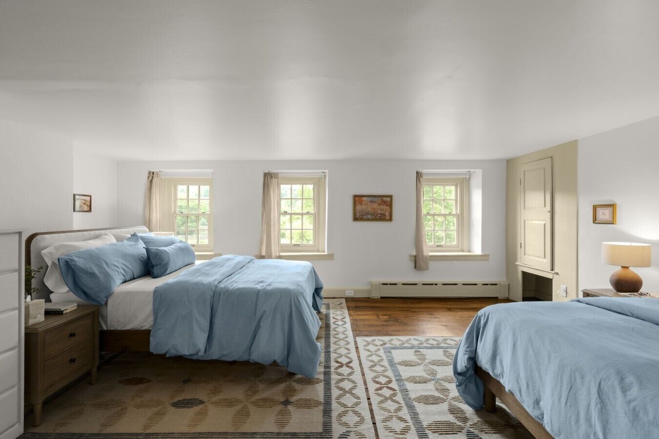 A bedroom with two beds, a nightstand, a dresser, a window with curtains, a radiator, and a lamp.