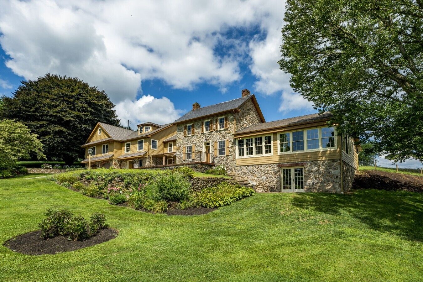 A large, multi-story stone house with a well-maintained lawn and garden.