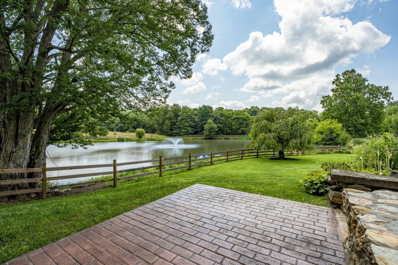 A brick patio with a view of a lake and a wooden fence.