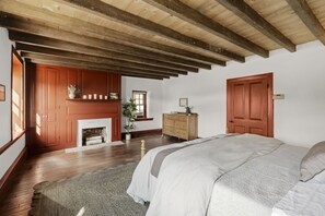 Une chambre avec un plafond en bois, une cheminée, un lit et une commode.