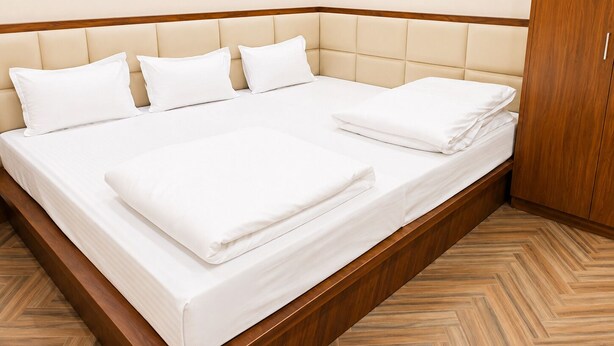 A neatly made bed with a wooden headboard and a herringbone-patterned floor. - Hotel Char Dham Inn - Varanasi (Varanasi)