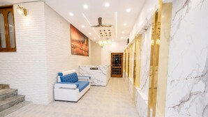 A reception area with a reception desk, a seating area with a sofa and armchairs, and a marble wall. - Hotel Char Dham Inn - Varanasi (Varanasi)