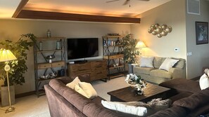 Ein Wohnzimmer mit Flachbildfernseher, Holzbögen, einer Couch, einem Couchtisch und einer Lampe.
