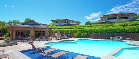 A resort with a large swimming pool, lounge chairs, and a covered patio area.
