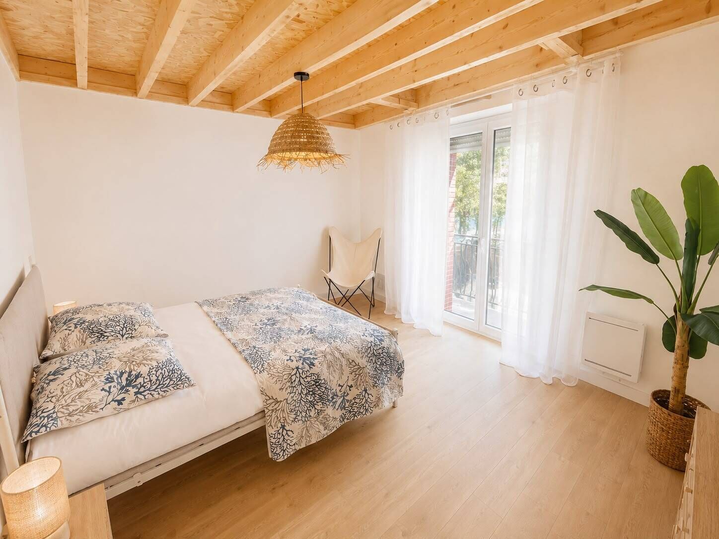 A bedroom with a bed, a chair, a hanging light fixture, and a potted plant.