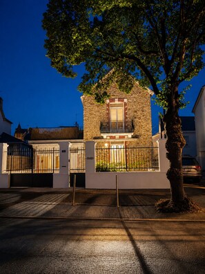 Un bâtiment en pierre doté d’un balcon, d’une entrée fermée par un portail et d’un arbre devant.