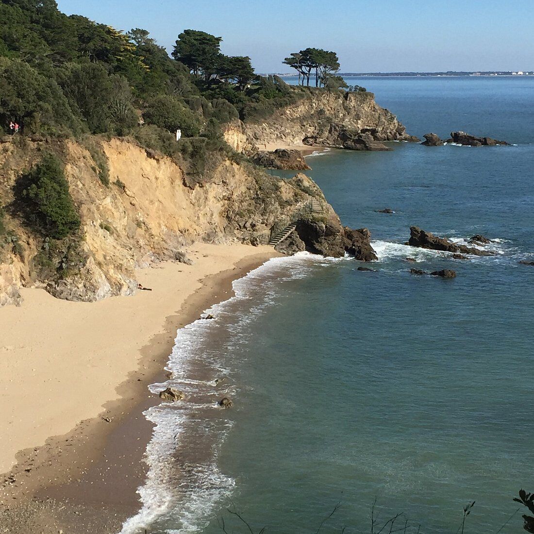 A coastal landscape with a sandy beach, rocky cliffs, and a clear view of the sea.