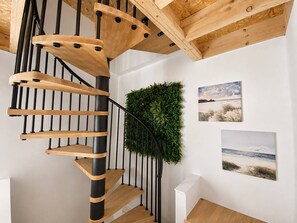 A spiral staircase with wooden steps and black balusters, a green wall-mounted plant, and two framed pictures on the wall. - Villa Océa 1900 face mer, terrasse panoramique (Saint-Nazaire)