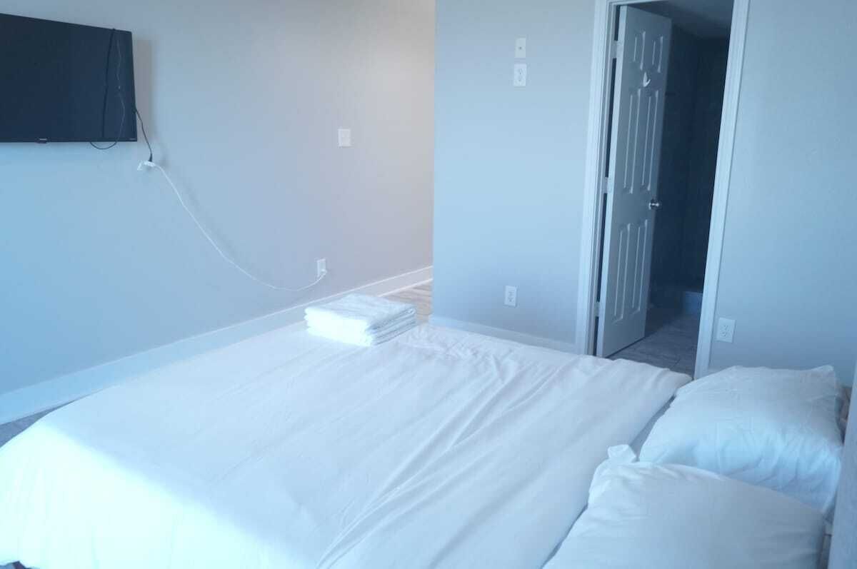 A room with a bed, a flat-screen TV mounted on the wall, and a door leading to another room.