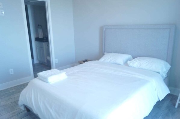 Une chambre à coucher comprenant un lit, une table de chevet et une porte donnant sur une salle de bain.