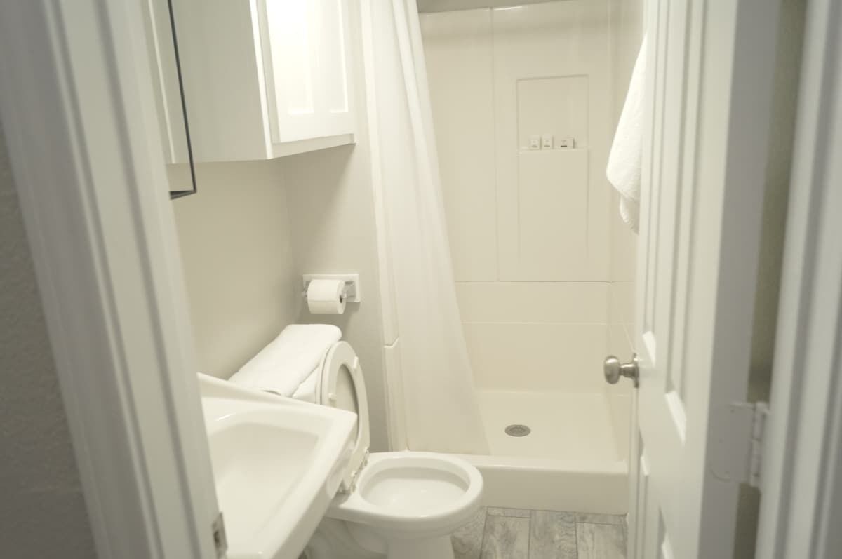 Ein kleines, weißes Badezimmer mit Toilette, Duschkabine und Waschbecken.