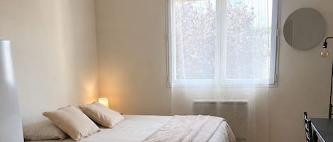 A bedroom with a bed, bedside table, and a window with curtains.