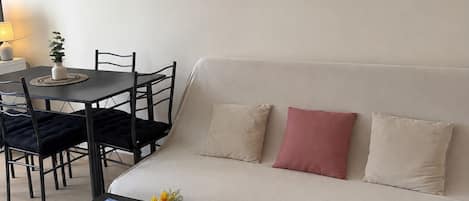 A living room with a sofa, a coffee table, a dining table with chairs, and a small plant on the wall.