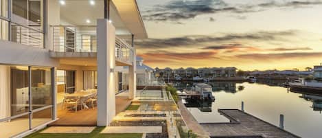 A modern two-story house with a glass balcony overlooking a marina.