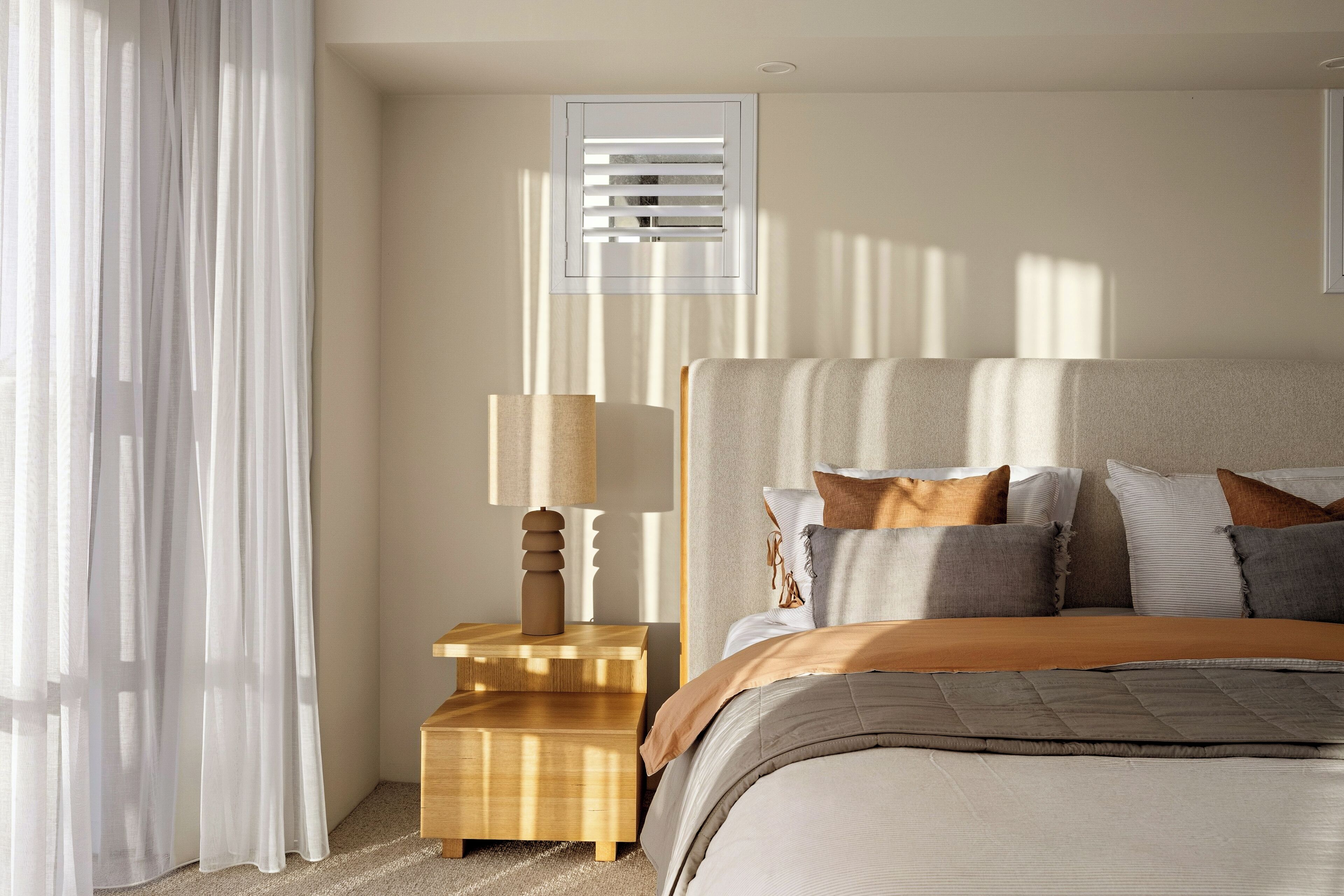 Ein Schlafzimmer mit Bett, Nachttisch, Lampe und einem Fenster mit Jalousien.