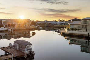 A marina with boats docked, a covered boat, and houses in the background during sunset. - Luxury 5BR canal retreat with private jetty, alfresco, water views & space for 10. (Dudley Park)