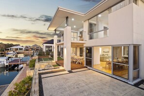 A modern two-story house with a balcony, a dining area, and a view of the water. - Luxury 5BR canal retreat with private jetty, alfresco, water views & space for 10. (Dudley Park)