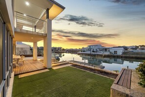 A modern house with a balcony overlooking a body of water and a sunset. - Luxury 5BR canal retreat with private jetty, alfresco, water views & space for 10. (Dudley Park)