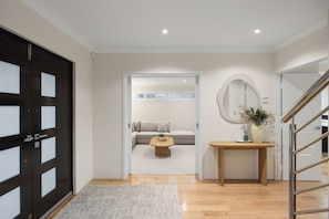 A modern interior with a black door, a hallway leading to a living area with a sofa and coffee table, and a round mirror on the wall. - Luxury 5BR canal retreat with private jetty, alfresco, water views & space for 10. (Dudley Park)