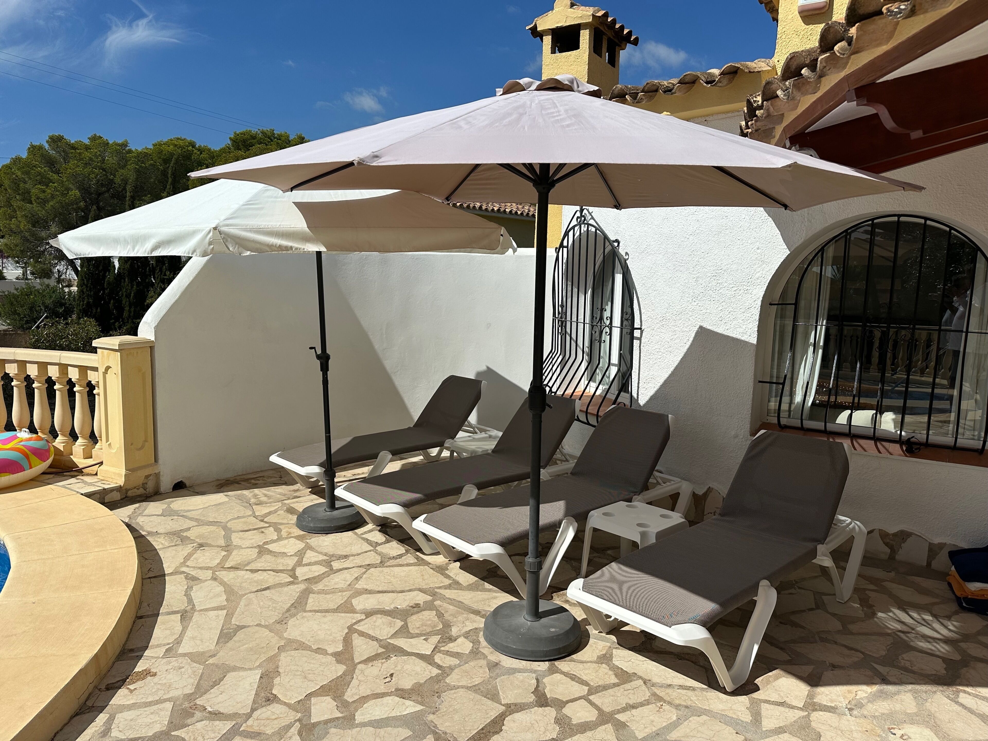 Une terrasse avec des chaises longues, un grand parasol et une piscine.