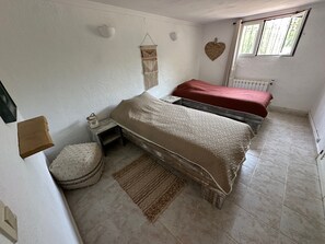 A bedroom with two beds, a small bedside table, a round ottoman, a wall-mounted light fixture, a heart-shaped decoration, and a window with a view. - Villa Helios - Within walking distance of Moraira - plenty of space and privacy (Teulada)
