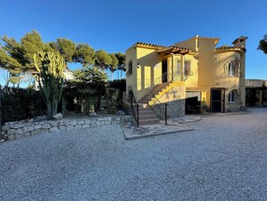 A yellow building with a stone wall, a staircase, and a gravel courtyard. - Villa Helios—Private Pool—Walking Distance to Moraira Center—Plenty of Space and Privacy (Teulada)