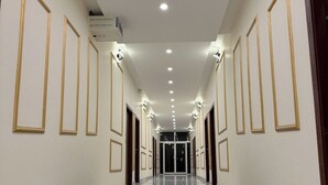 A hallway with a green carpet, white walls, and gold-framed picture frames. - Hard Rock Hotel (Islamabad)