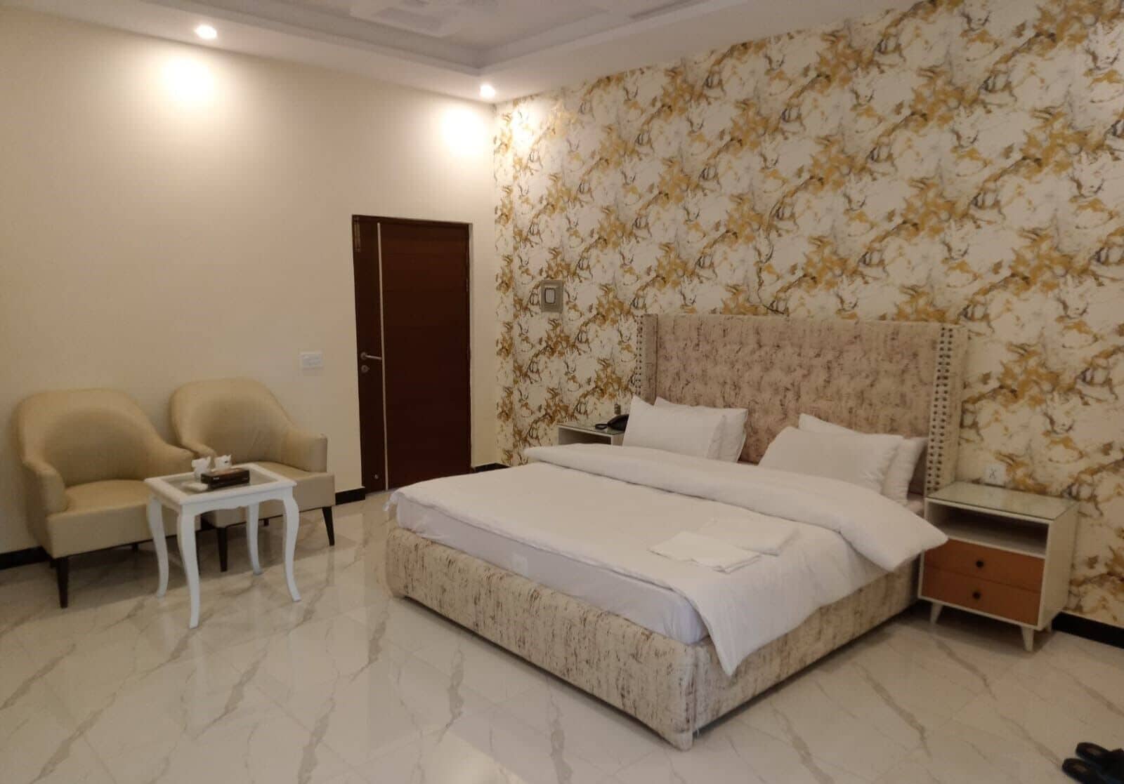 A hotel room with a large bed, two armchairs, a small table, a nightstand, and a door.