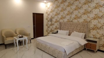 A hotel room with a large bed, two armchairs, a small table, a nightstand, and a door.