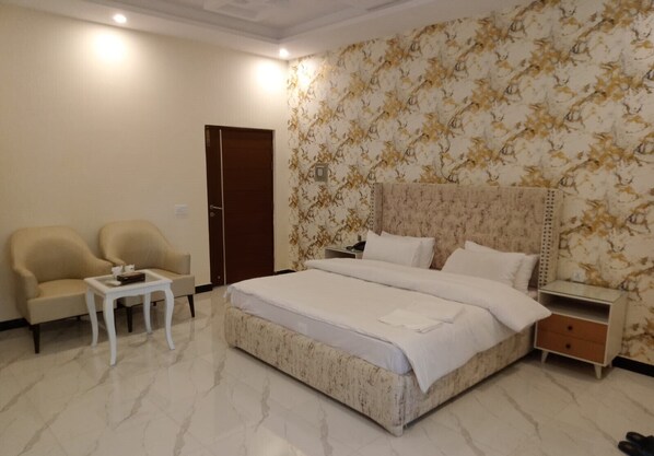 A hotel room with a large bed, two armchairs, a small table, a nightstand, and a door.