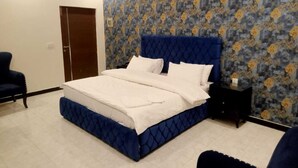 A bedroom with a large bed, a nightstand, a chair, and a patterned wallpaper. - Hard Rock Hotel (Islamabad)