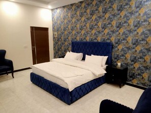 A bedroom with a large bed, a nightstand, a chair, and a patterned wallpaper.