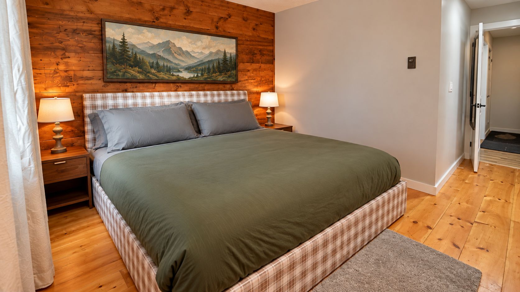 Un dormitorio con cabecera de madera, cama con colcha verde, dos lámparas de noche y un cuadro de un paisaje montañoso.