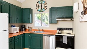 Eine Küche mit taubenblauen Schränken, einem weißen Kühlschrank, einer Mikrowelle, einer Kaffeemaschine, einem Wasserkocher und einem Geschirrspüler.