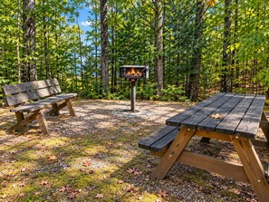 Ein Picknickplatz mit Feuerstelle, Bänken und einem Tisch, umgeben von Bäumen.