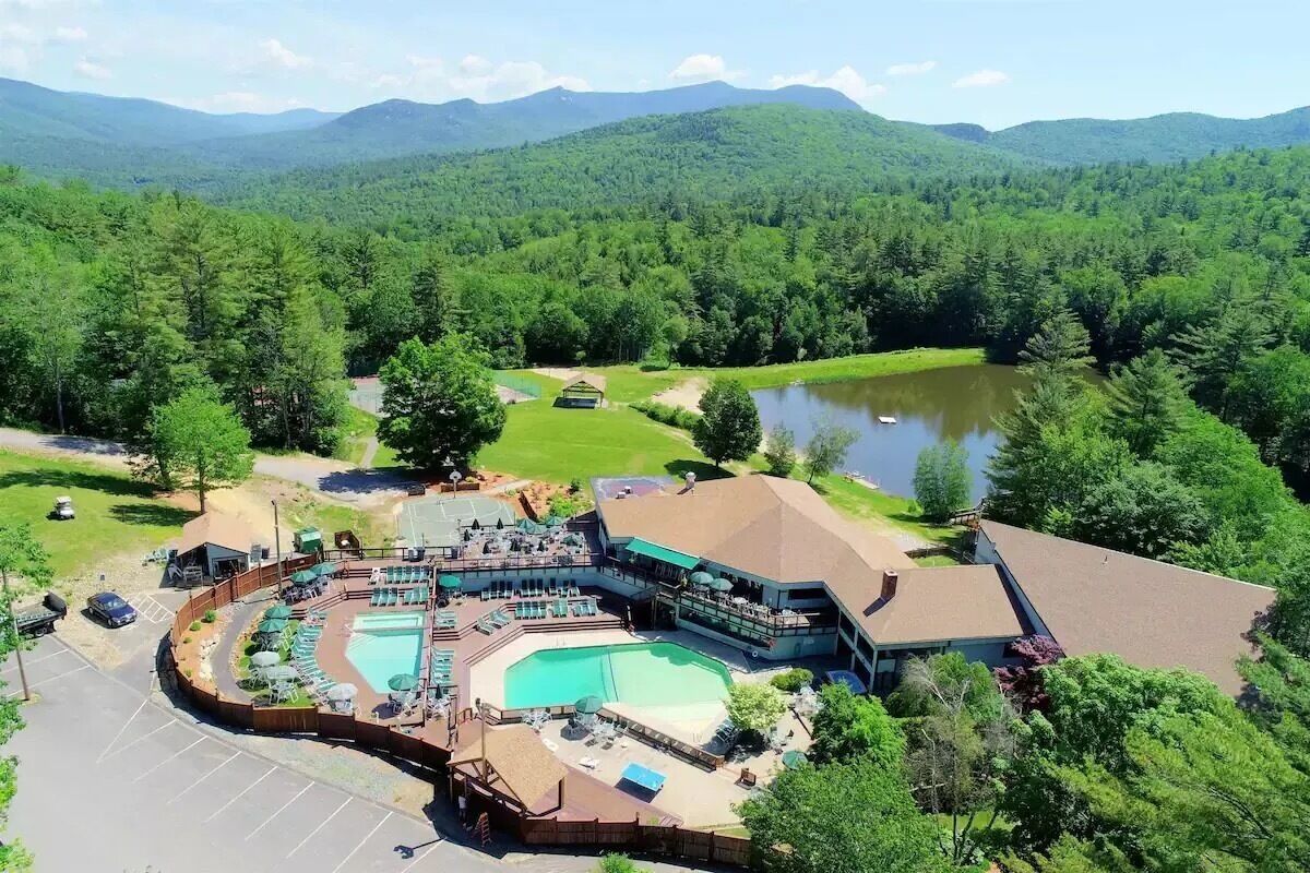 A resort with a large pool, outdoor seating, and a view of the surrounding forest and mountains.