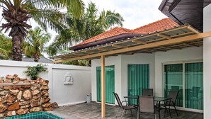 Ein Poolbereich mit Steinmauer, einer Pergola und einer Sitzecke mit Stühlen und einem Tisch.