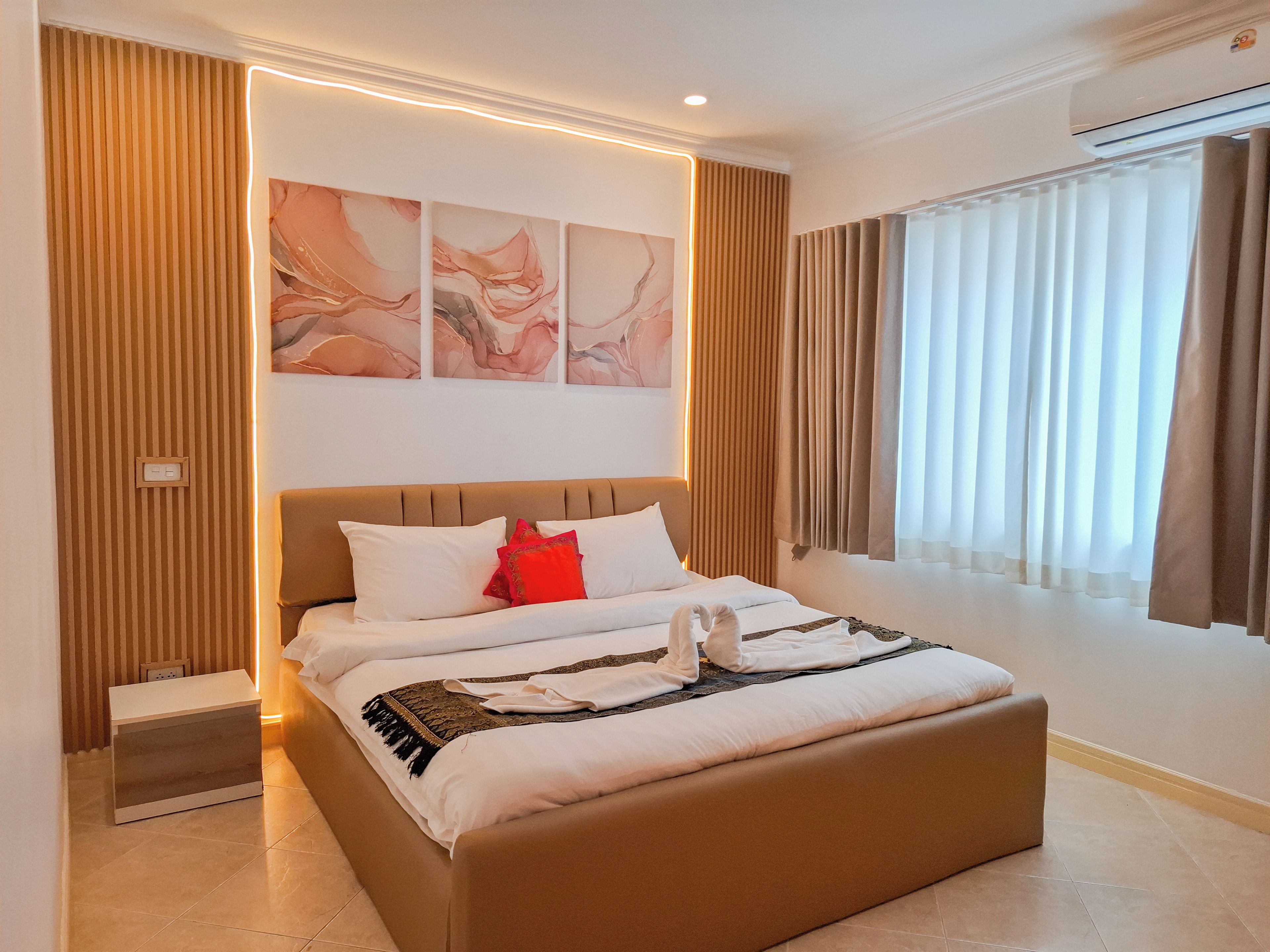 A modern hotel room with a large bed, a bedside table, a wall-mounted air conditioning unit, and a window with curtains.
