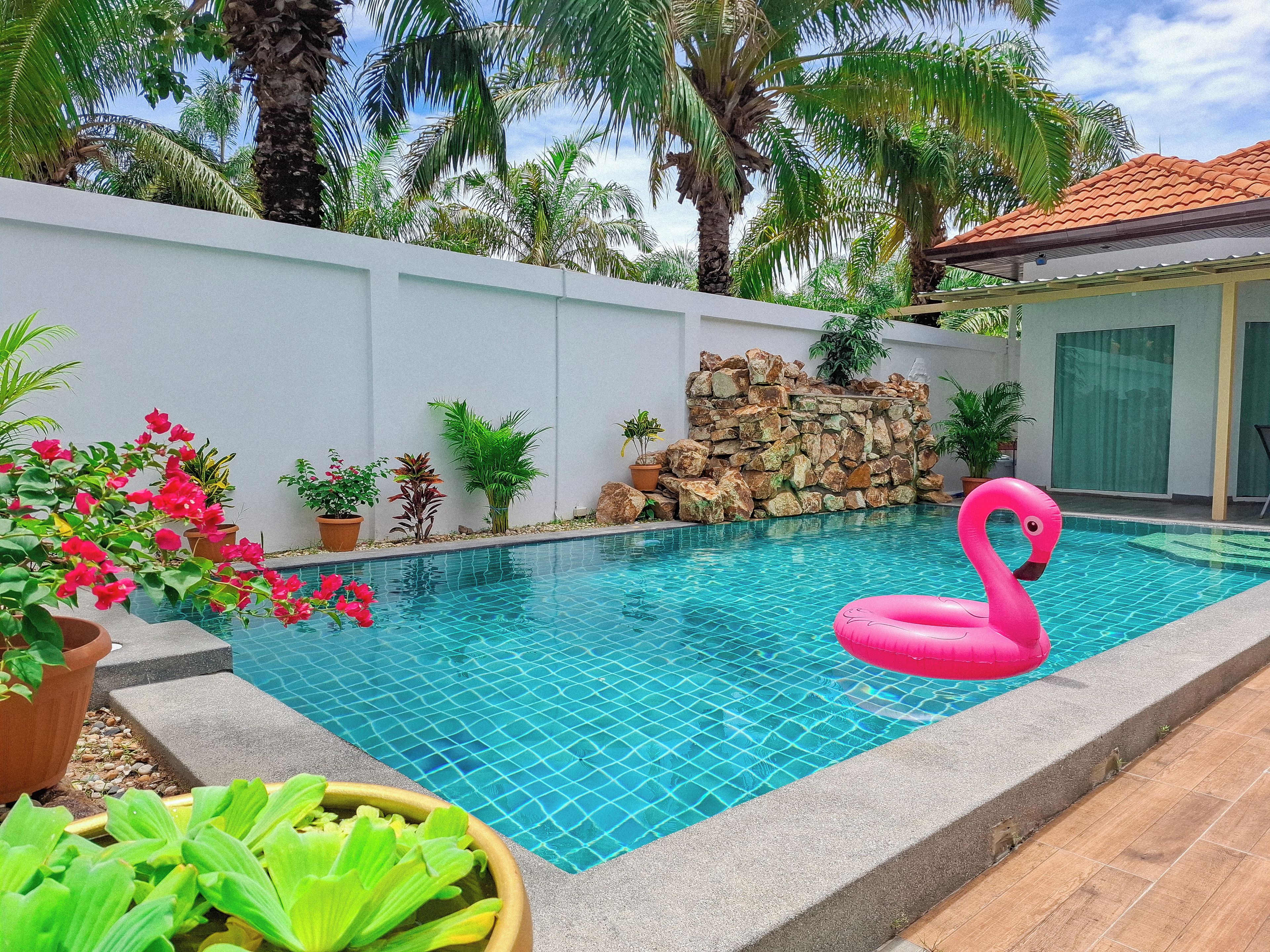 An indoor swimming pool with a pink flamingo float, surrounded by potted plants and a stone wall.