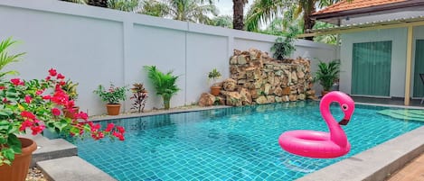 An indoor swimming pool with a pink flamingo float, surrounded by potted plants and a stone wall.