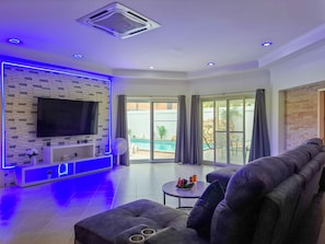 Ein modernes Wohnzimmer mit Flachbildfernseher, einer Sitzecke mit Sofa, einem kleinen Tisch mit Getränken und einem Balkon mit Blick auf einen Pool.