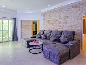 A modern living room with a sectional sofa, a round coffee table, and a stone wall. - Beachside 4BR Private Pool Villa  (Muang Pattaya)
